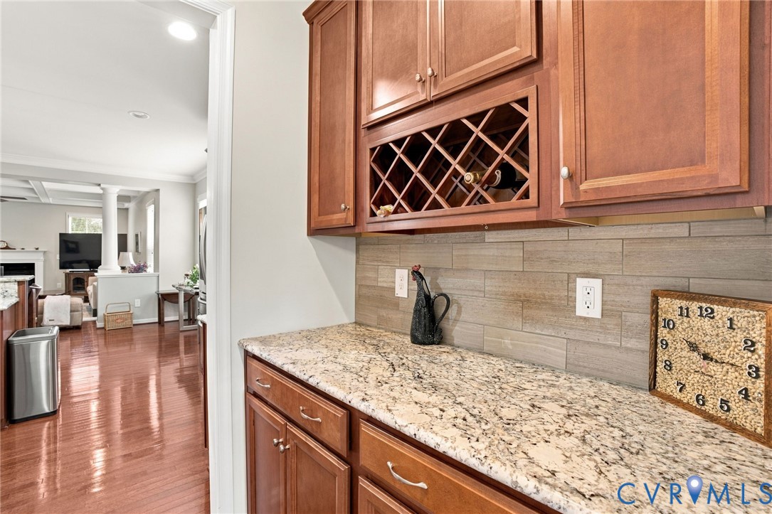 Wood-finish cabinetry with a built-in wine rack, light-toned stone-finish countertop, and horizontal tile backsplash