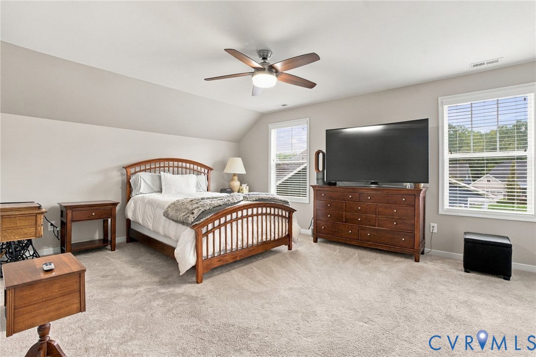 Spacious room with sloped ceilings, light-colored carpeting, multiple windows, and a ceiling fan