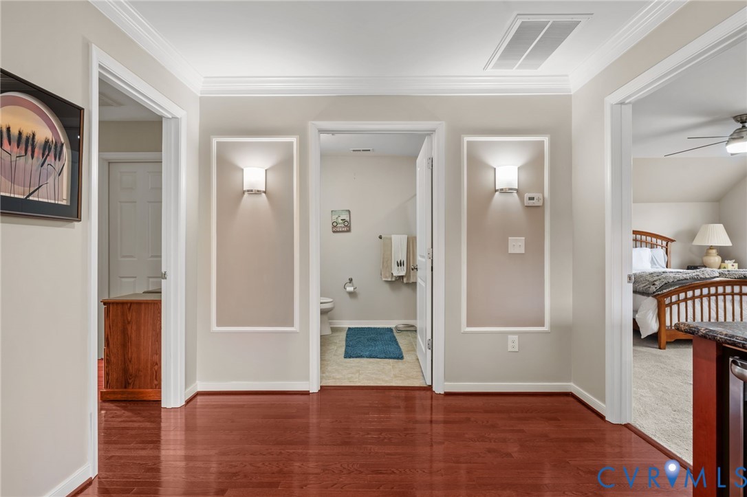 Wood-finish flooring, crown molding, wall sconces, and white trim accents