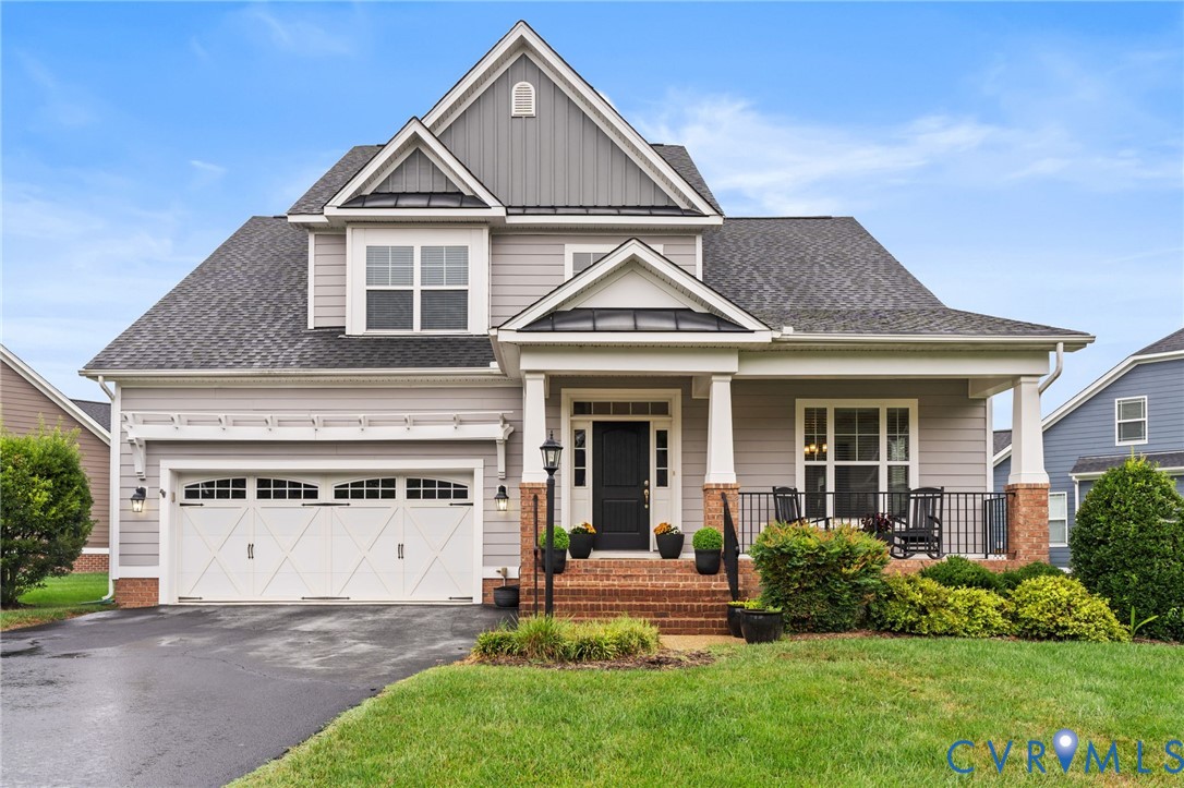 Traditional-style residence featuring a covered front porch, brick accents, and a two-car garage with decorative doors Traditional-style residence featuring a covered front porch, brick accents, and a two-car garage with decorative doors