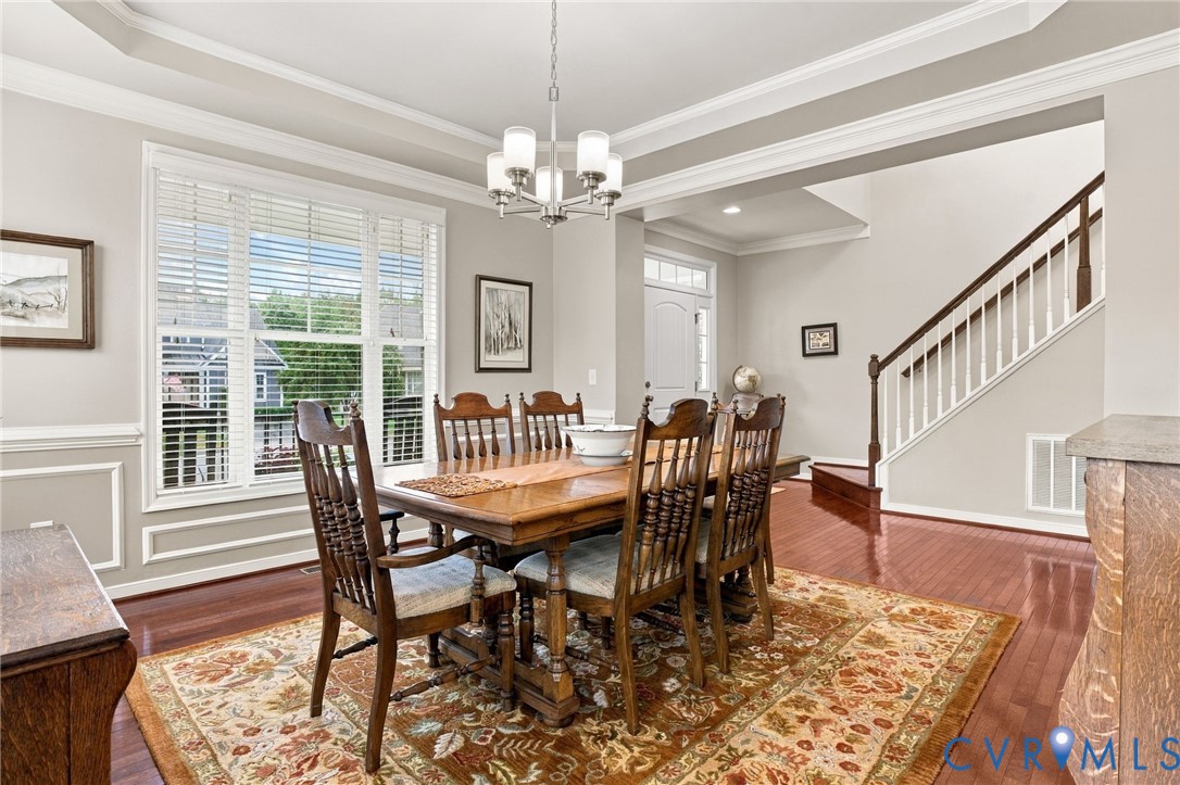 Tray ceiling with crown molding, wainscoting, large windows, wood-finish flooring, and a staircase with white balusters