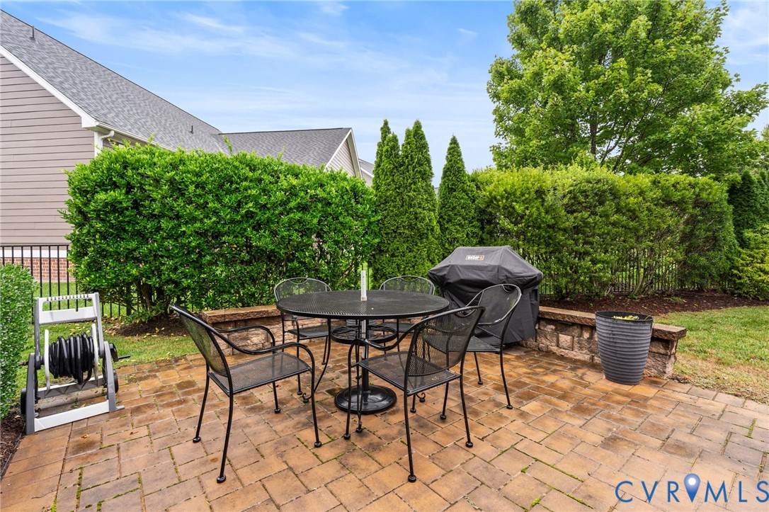 Brick paver patio featuring a low stone retaining wall and mature perimeter shrubbery