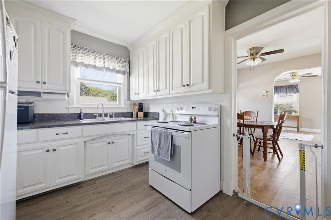 Kitchen featuring white cabinetry, dark countertops, a stainless steel sink with a gooseneck faucet, and wood-finish flooring