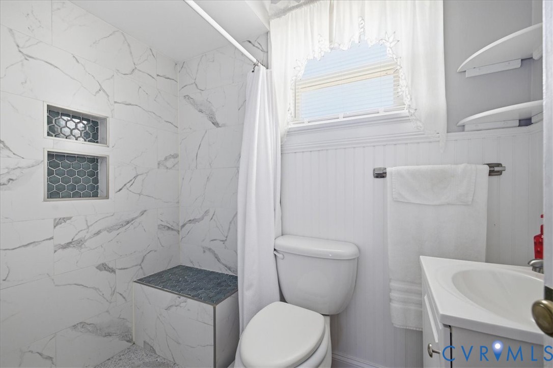 Walk-in shower with marble-look tile, built-in shelving, and tiled bench