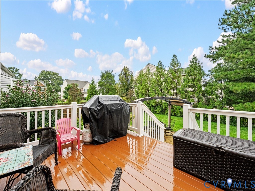 Expansive rear deck with wood-finish surface, white railings, and integrated stairs to a manicured lawn
