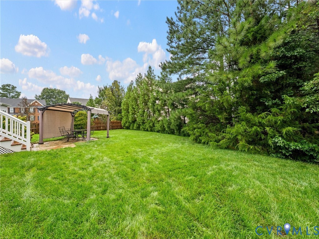 Expansive green lawn with mature perimeter trees, a white railing staircase, and a covered outdoor patio area