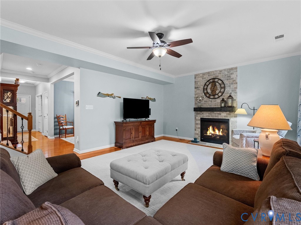 Built-in fireplace with a stone surround and wood mantel, ceiling fan with integrated lighting, crown molding, and wood-finish flooring