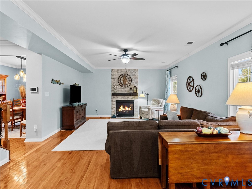 Hardwood flooring, crown molding, ceiling fan, and a fireplace with a stone surround