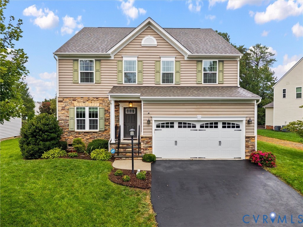 Two-story residence featuring stone and siding facade, double garage, front door with sidelights, and mature landscaping