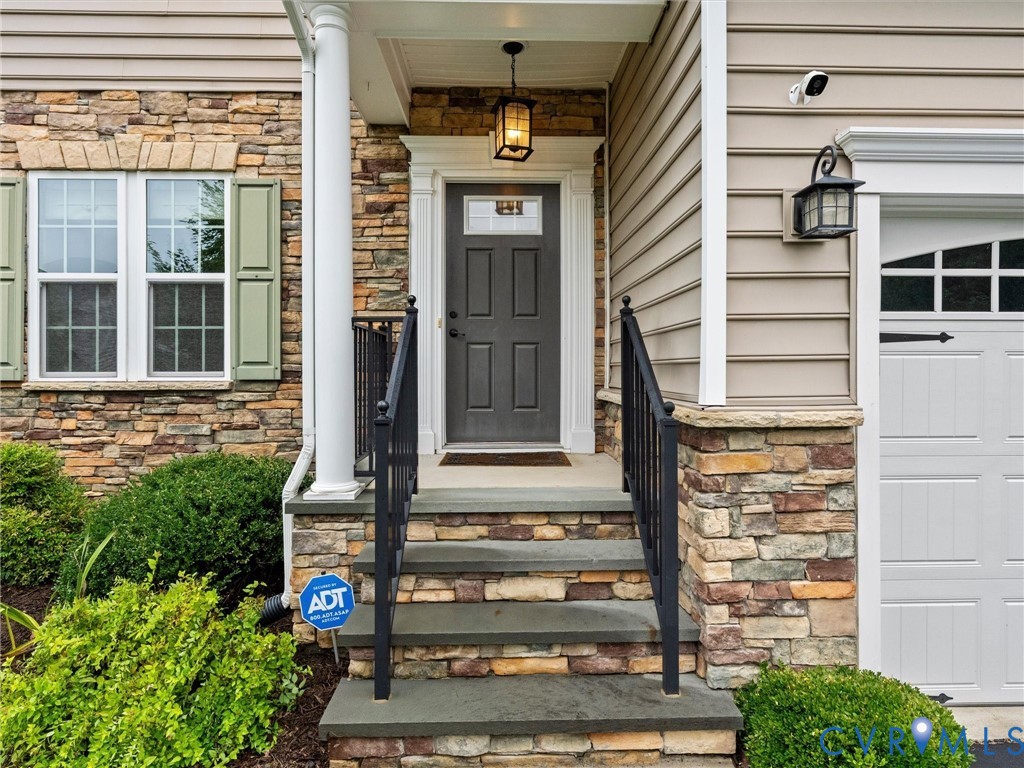 Entry with stone facade, decorative column, and dark gray paneled door with transom window