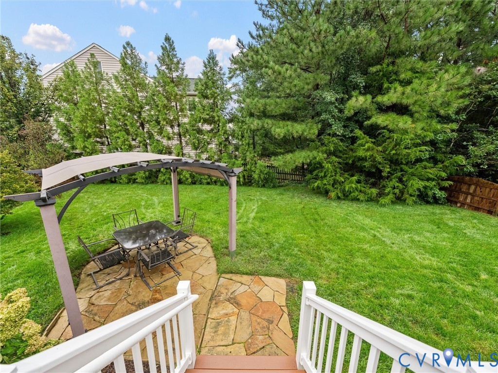 Expansive backyard featuring a natural flagstone patio, pergola with a fabric canopy, and mature trees providing privacy