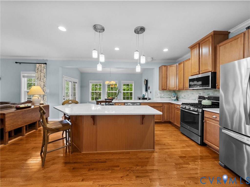 Hardwood flooring, wood-finish cabinetry, stainless steel appliances, central island with solid surface countertop, and recessed lighting