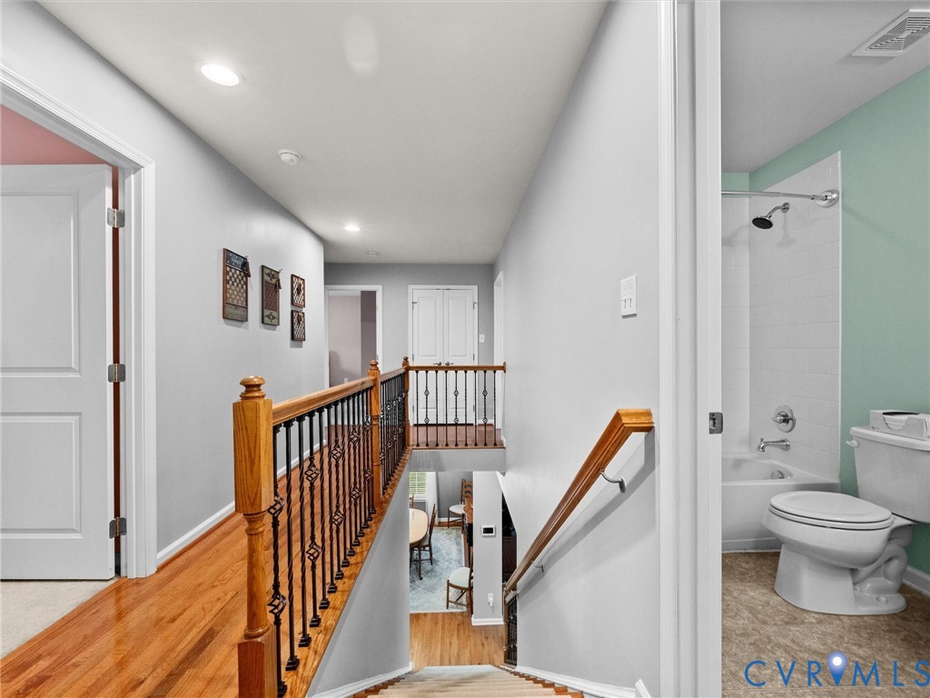 Recessed lighting, wood-finish flooring, staircase with wrought iron balusters, and a full bathroom with a tub/shower combination