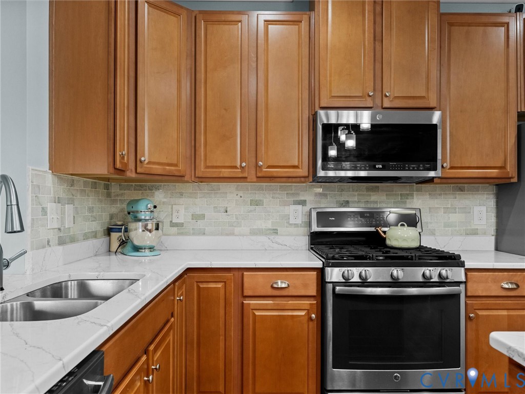 Wood-finish cabinetry, stainless steel appliances, white countertop, and tiled backsplash