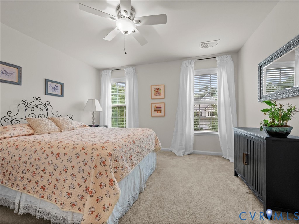 Light neutral wall paint, ceiling fan with integrated lighting, two windows with blinds, and neutral carpeting
