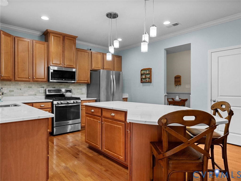 Kitchen featuring wood-finish cabinetry, stainless steel appliances, a center island with countertop seating, and recessed lighting