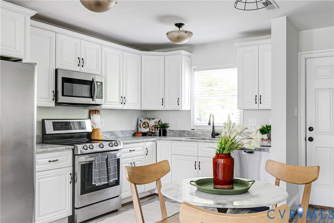 White shaker-style cabinetry with dark hardware, stainless steel appliances, grey veined countertops, and a built-in kitchen sink