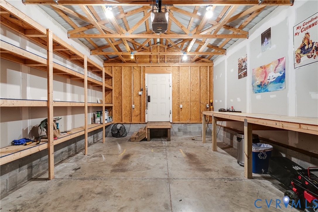 Garage featuring exposed wood beam ceiling, concrete floor, overhead lighting, extensive built-in shelving, and a built-in workbench