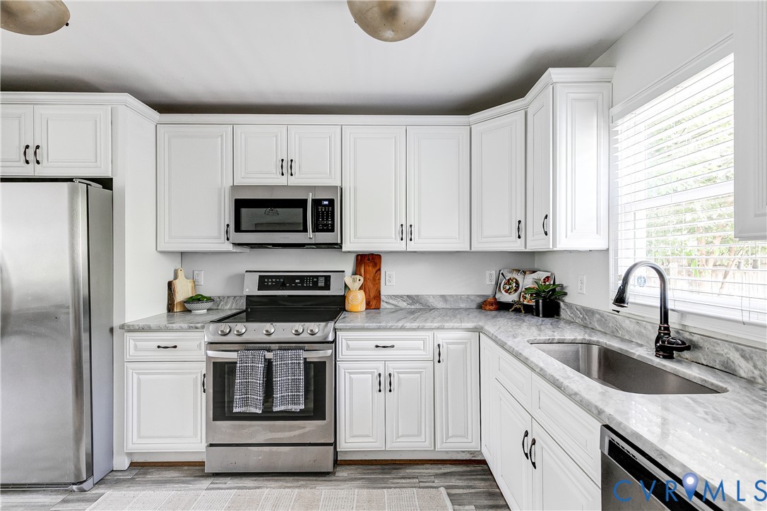 White cabinetry with dark hardware, stainless steel appliances, undermount sink with gooseneck faucet, light-toned countertops, and wood-finish flooring