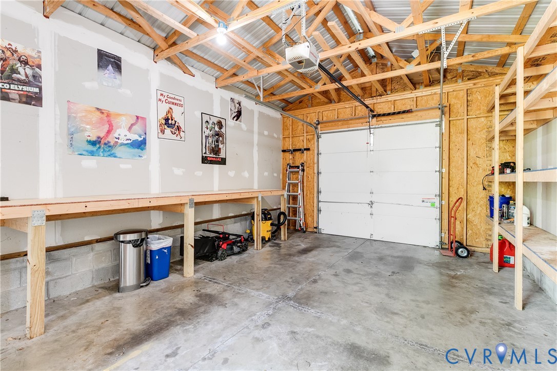 Garage space featuring exposed wood rafter ceiling, concrete flooring, built-in wooden shelving, a built-in wooden workbench, and an overhead garage door with an automatic opener