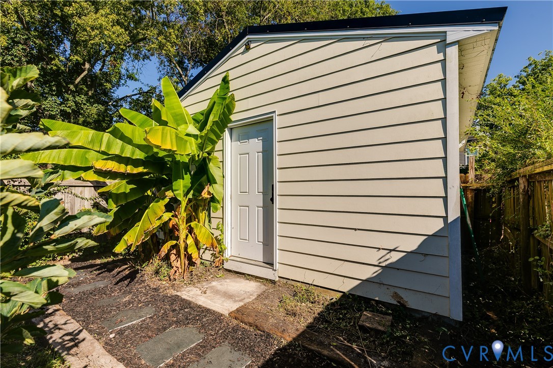 Exterior storage structure with horizontal siding, a single panel door, and a dark-colored sloped roof