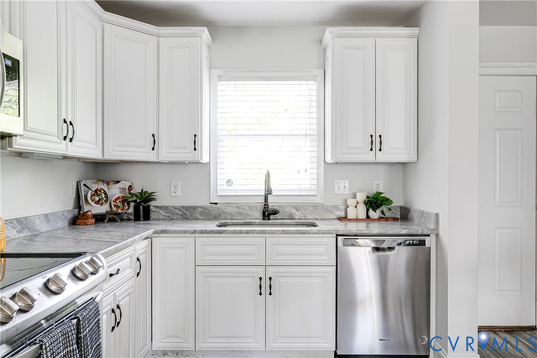 White shaker-style cabinetry, stainless steel dishwasher, undermount sink with a gooseneck faucet, and light-toned countertops