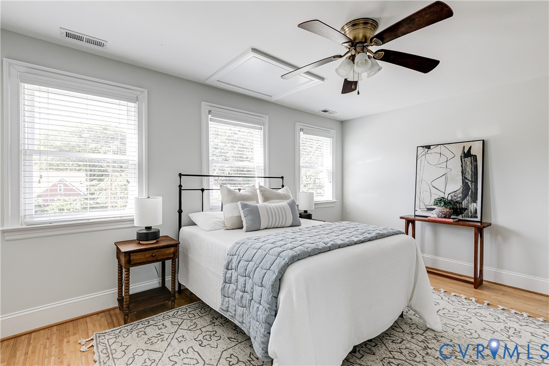 Bright room with wood-finish flooring, multiple windows with blinds, a ceiling fan, and white walls