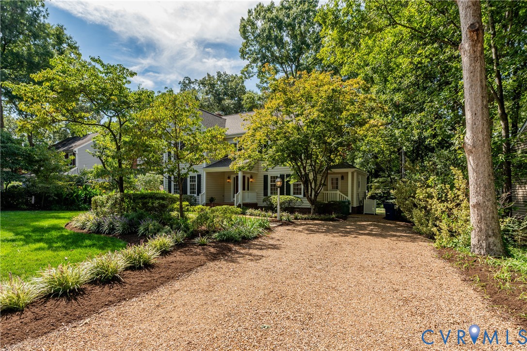 Gravel driveway leading to a residence with a covered front porch, surrounded by mature trees and manicured landscaping Gravel driveway leading to a residence with a covered front porch, surrounded by mature trees and manicured landscaping