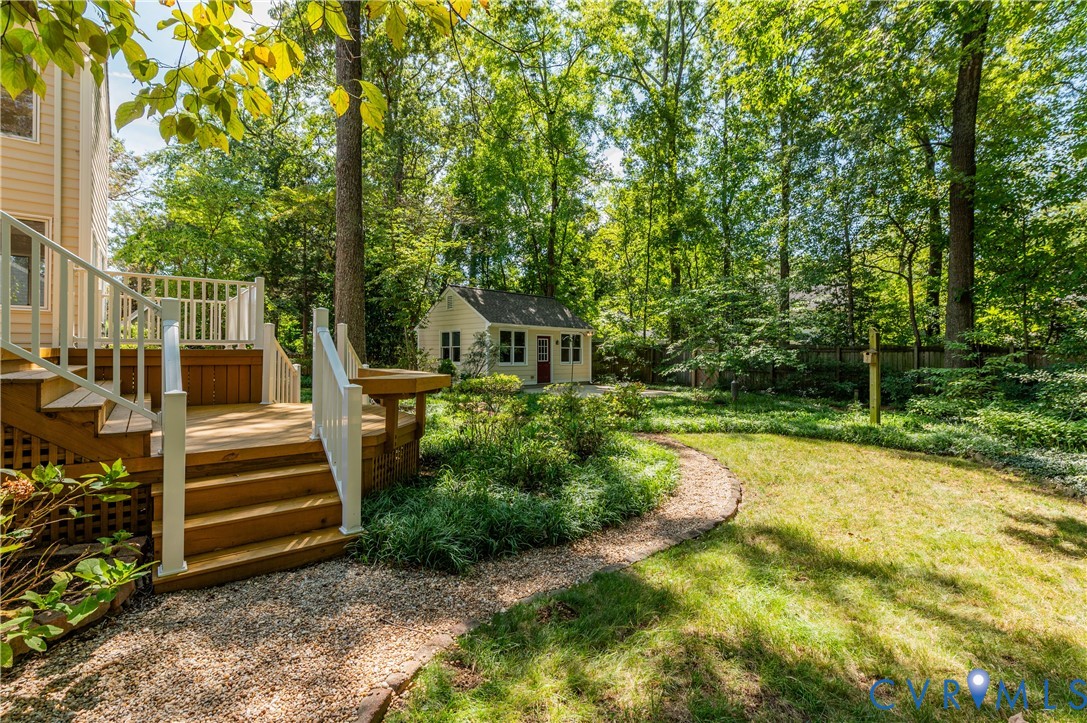 Wood deck with white railings, gravel path, manicured lawn, lush trees, and a detached shed