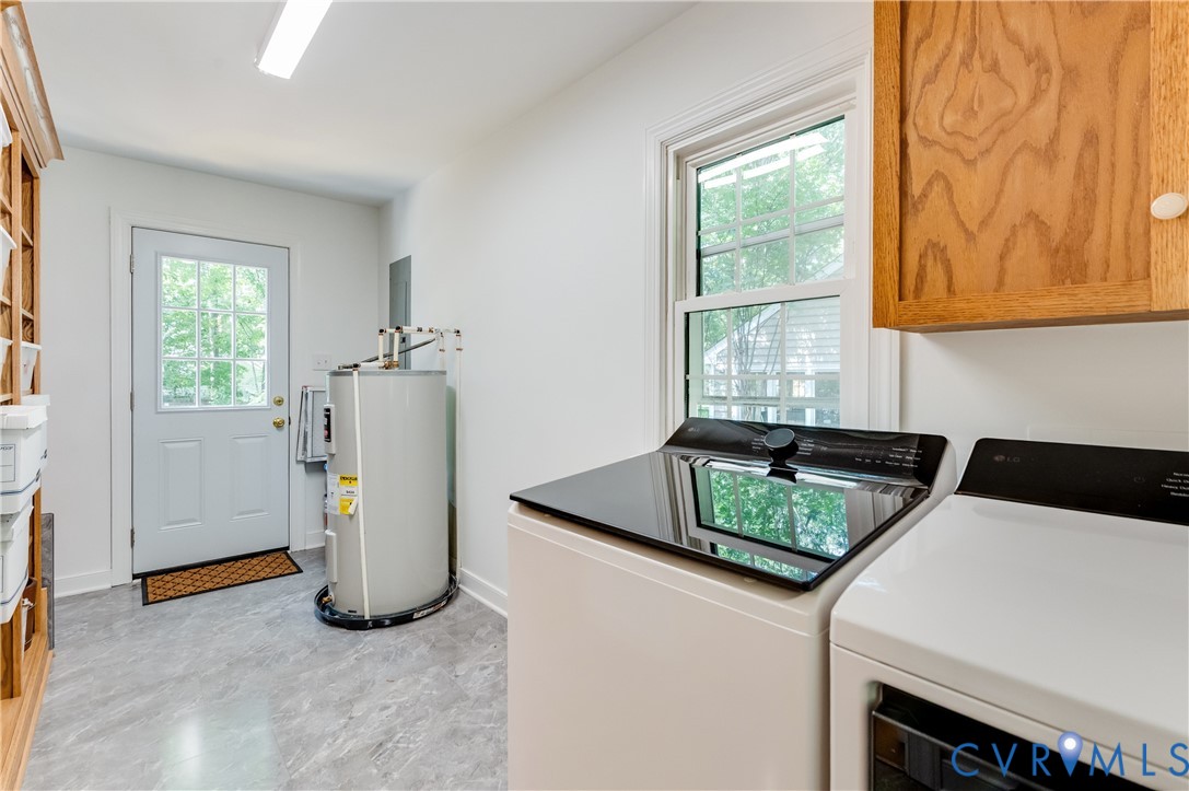 Utility space featuring grey stone-finish flooring, a white paneled door with glass inserts, a single-hung window with white trim, and light wood-tone cabinetry