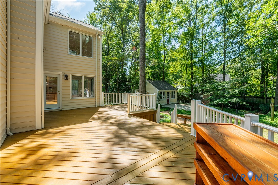 Expansive wood deck with white railing, leading to a detached shed and lush tree coverage
