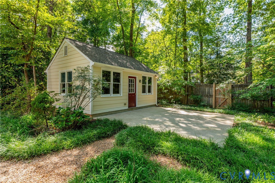 Light yellow siding with white trim, a dark red paneled door, multiple windows, a concrete patio, and a gravel pathway