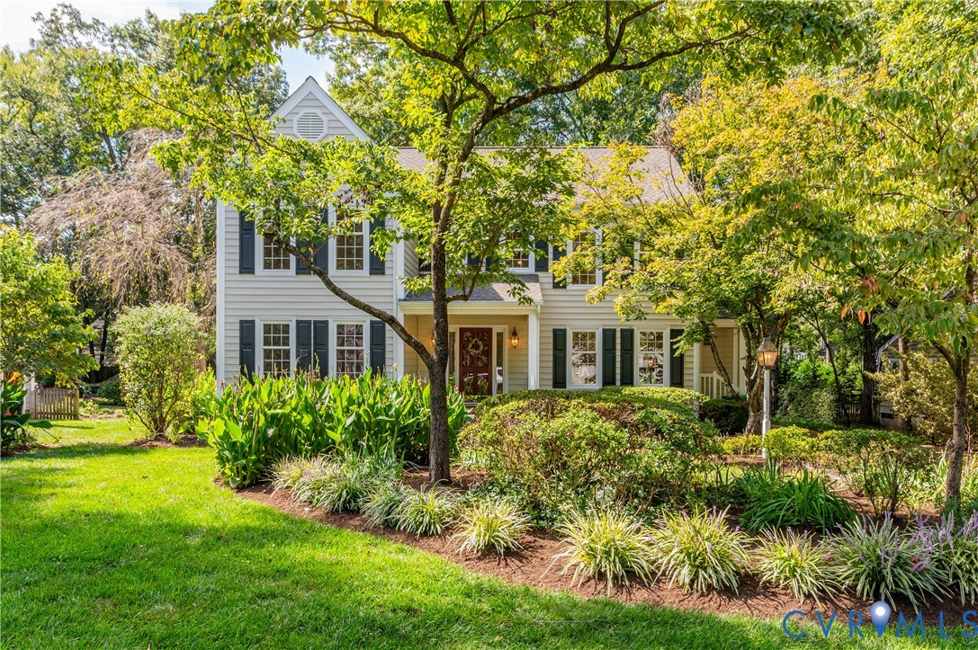 Two-story residence featuring light-colored siding, dark shutters, a covered front porch, and a dormer window Two-story residence featuring light-colored siding, dark shutters, a covered front porch, and a dormer window