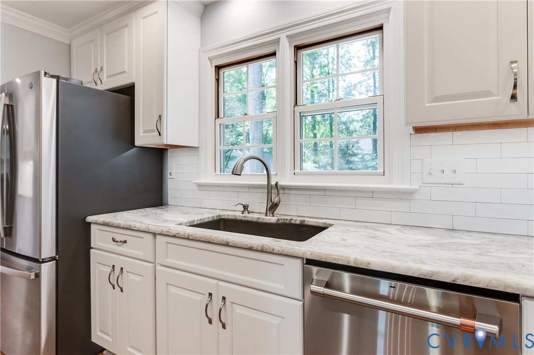 White shaker-style cabinetry, stainless steel appliances, undermount sink, stone countertop, and subway tile backsplash