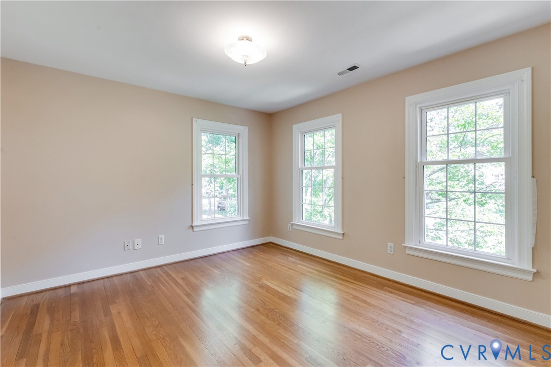 Hardwood flooring, three multi-pane windows, neutral wall tones, white trim, and a ceiling-mounted light fixture