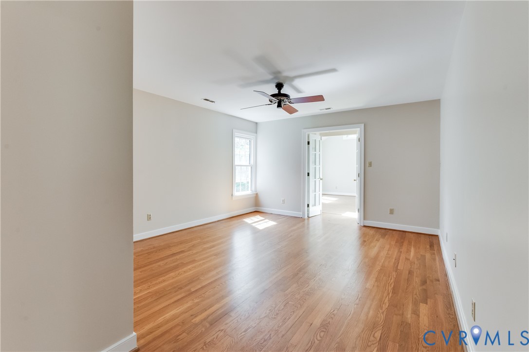 Hardwood flooring, white walls, ceiling fan, single window, and French doors