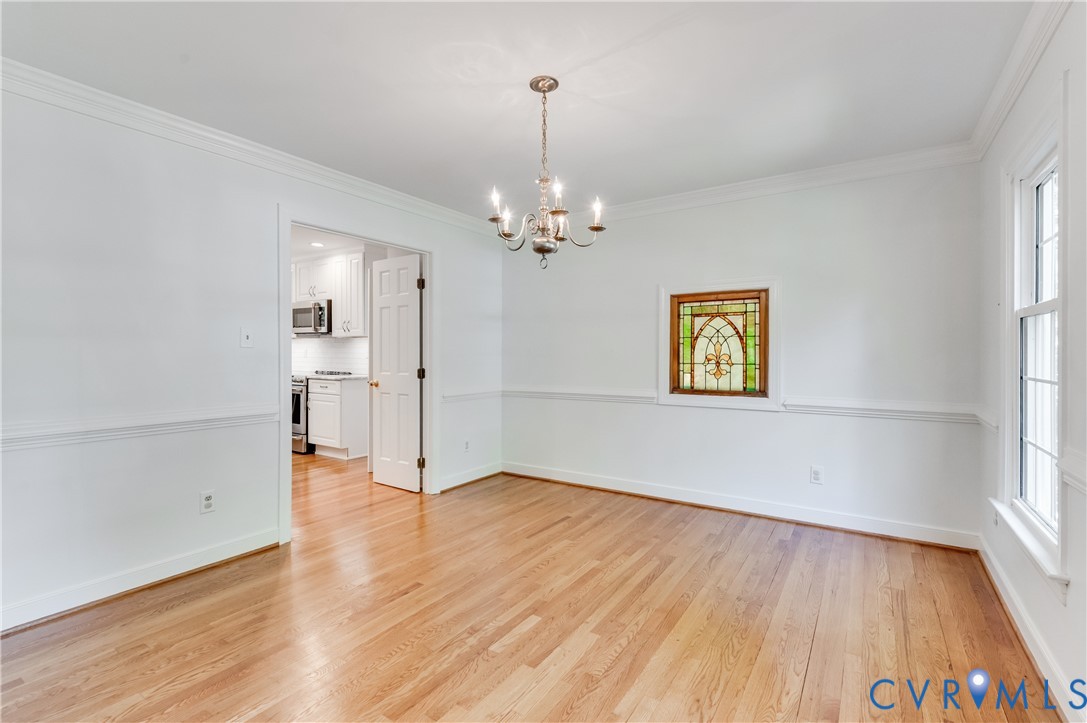 Hardwood flooring, decorative chandelier, stained glass window, crown molding, and chair rail detailing