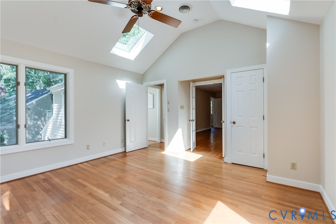 Vaulted ceiling featuring skylights and a ceiling fan, wood-finish flooring, and white trim