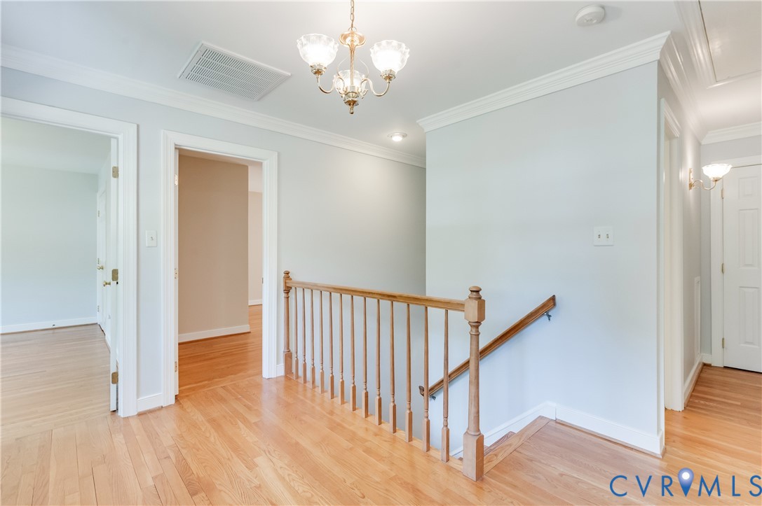 Hardwood flooring, crown molding, and a chandelier illuminate the upper landing