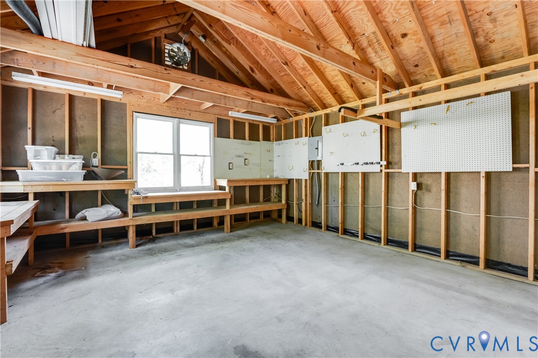 Open-concept attic space featuring exposed wood framing, concrete flooring, built-in shelving, a double window, and fluorescent lighting