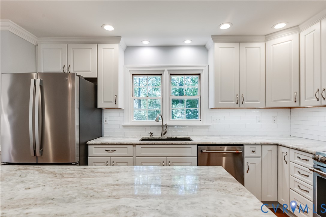 Updated kitchen featuring white shaker cabinetry, stainless steel appliances, white subway tile backsplash, and light-toned stone countertops