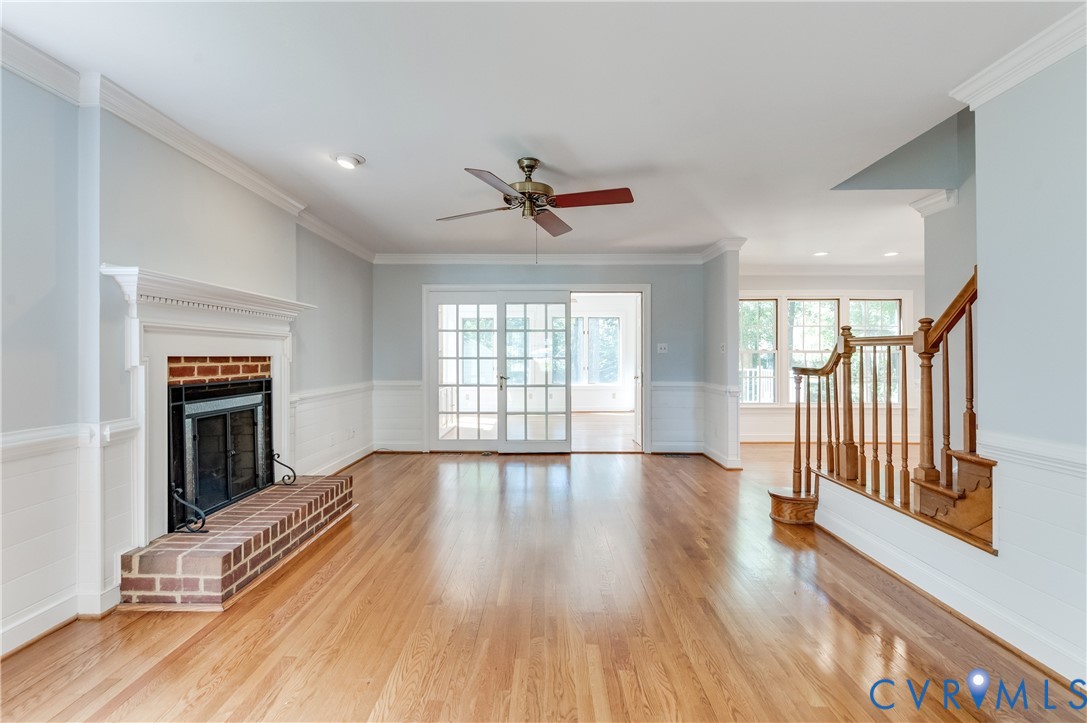 Hardwood flooring throughout, a brick fireplace with a white mantel, white wainscoting, and a ceiling fan