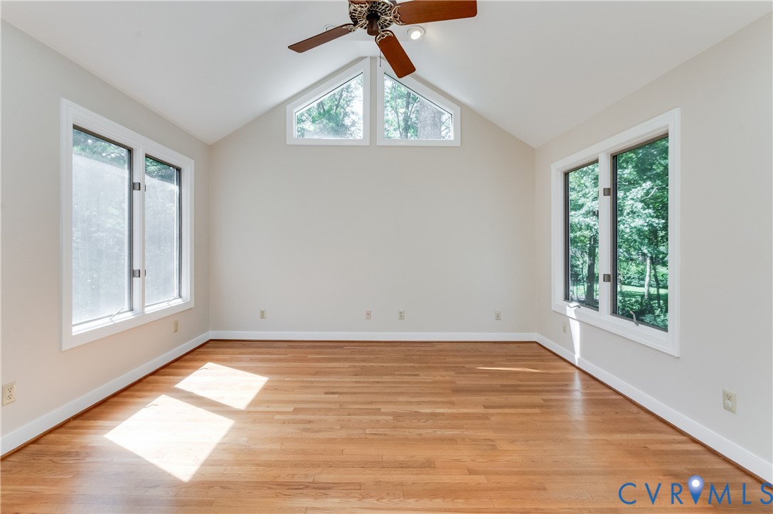 Vaulted ceiling, wood-finish flooring, ceiling fan, and multiple windows
