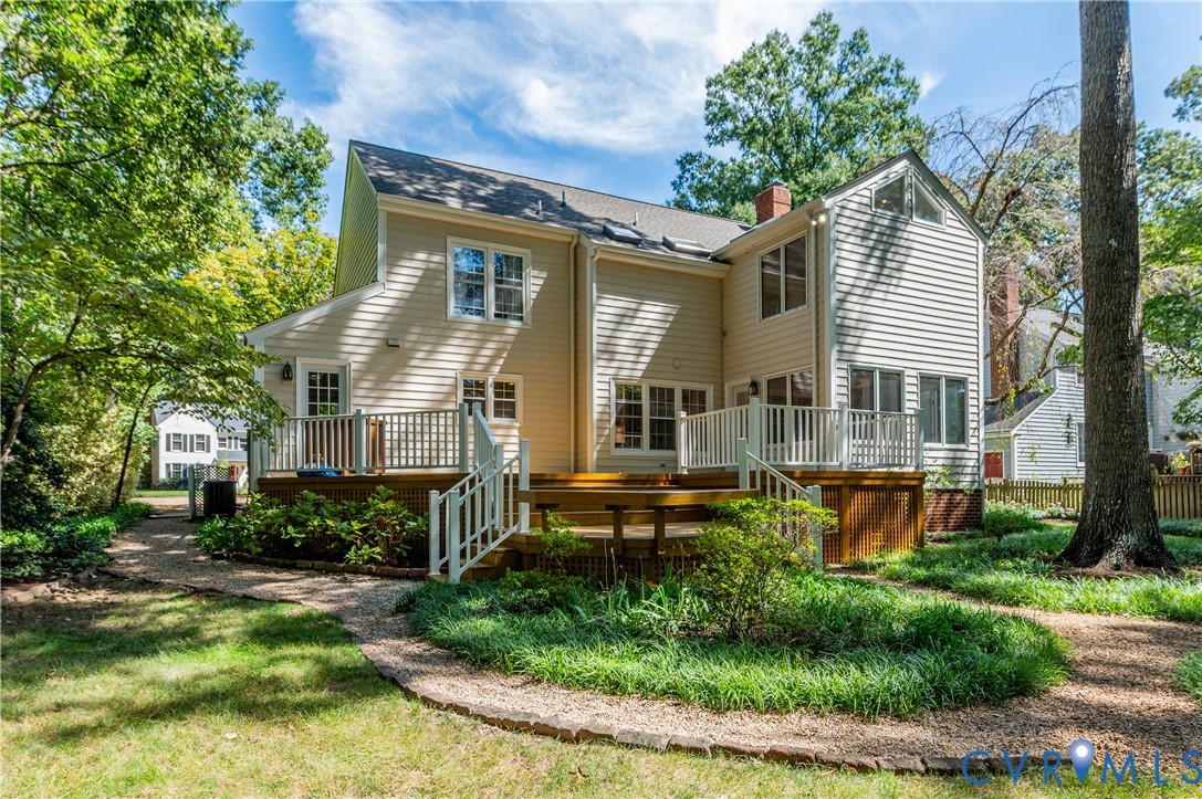 Multi-level wood deck with white railings, a brick chimney, and mature surrounding trees