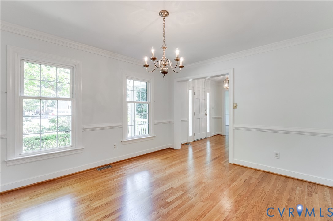Hardwood flooring, crown molding, chair rail molding, two large windows, and a classic chandelier