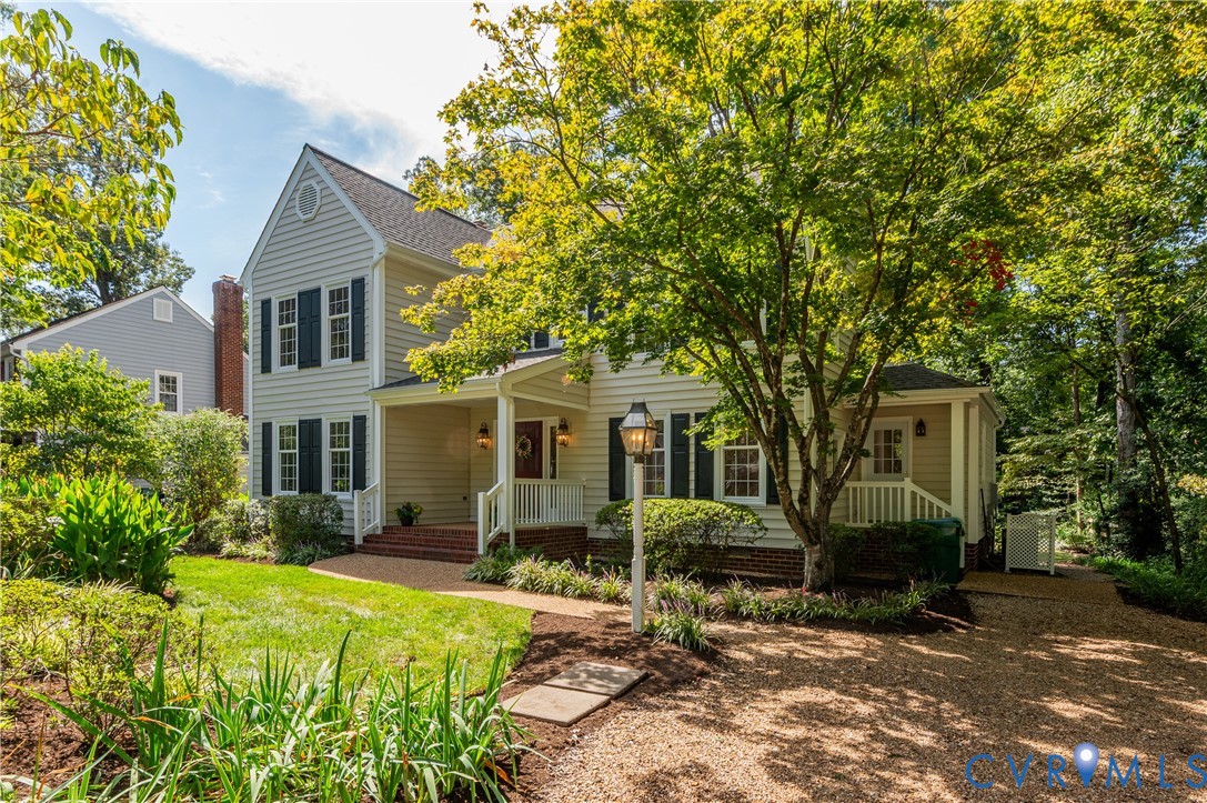 Traditional exterior with light siding and dark shutters, featuring a covered front porch with white railings, a gravel driveway, and a manicured lawn with mature trees Traditional exterior with light siding and dark shutters, featuring a covered front porch with white railings, a gravel driveway, and a manicured lawn with mature trees