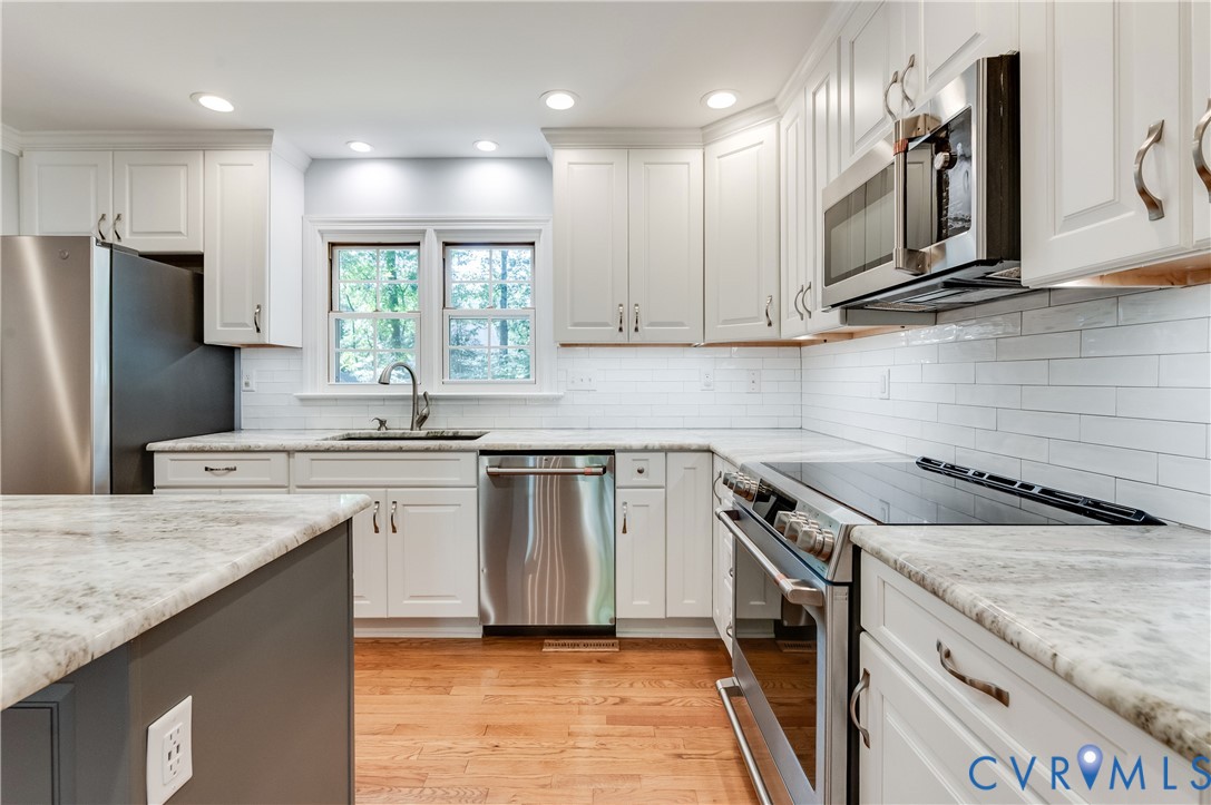 Kitchen featuring white cabinetry, light-toned countertops, stainless steel appliances, a subway tile backsplash, and wood-finish flooring