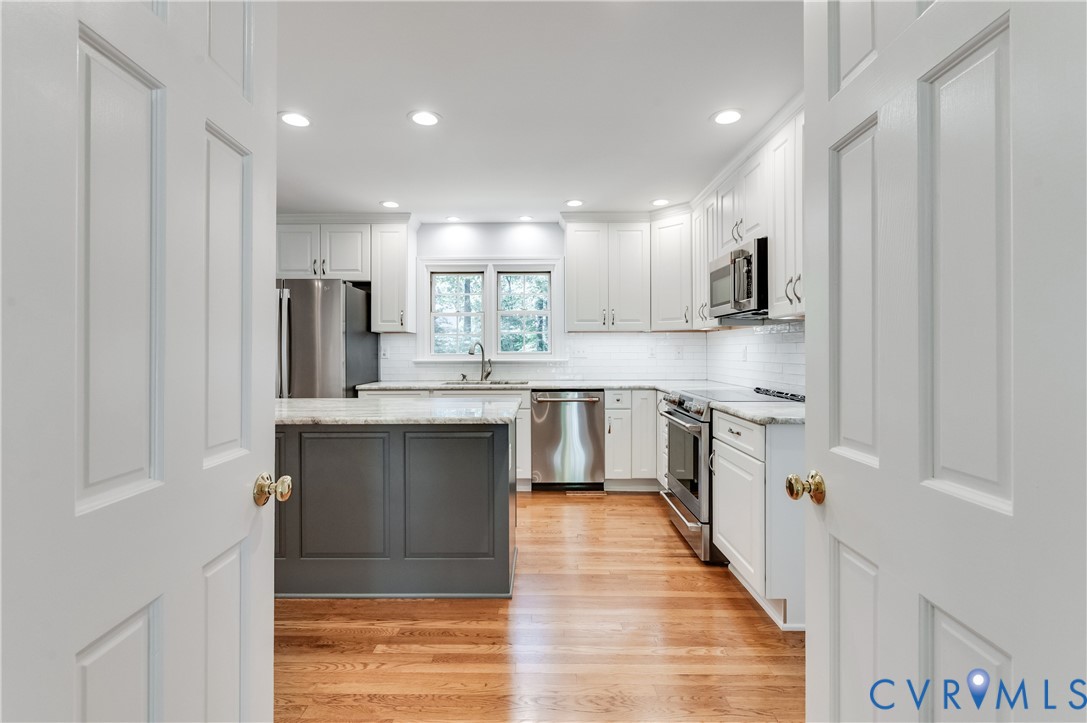 Renovated kitchen featuring a central island with a stone countertop, white shaker cabinetry, stainless steel appliances, wood-finish flooring, and recessed lighting