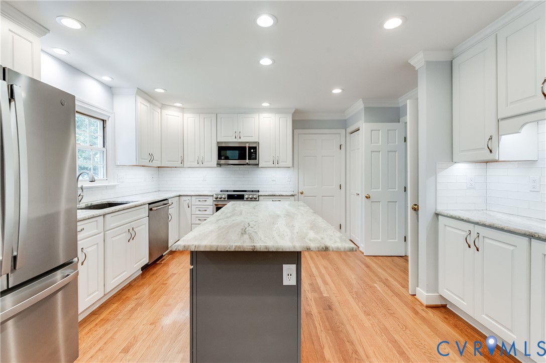 Kitchen featuring white cabinetry, stainless steel appliances, a center island with a light-toned countertop, hardwood flooring, and recessed lighting Kitchen featuring white cabinetry, stainless steel appliances, a center island with a light-toned countertop, hardwood flooring, and recessed lighting