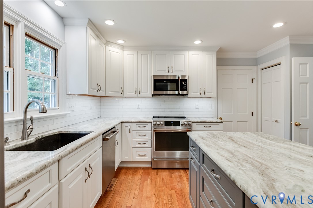 Kitchen featuring white shaker cabinetry, stainless steel appliances, light-toned countertops, subway tile backsplash, and hardwood flooring Kitchen featuring white shaker cabinetry, stainless steel appliances, light-toned countertops, subway tile backsplash, and hardwood flooring